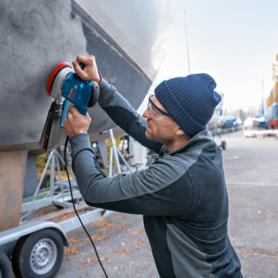 Homem lixando barco com lixadora elétrica azul no cais
