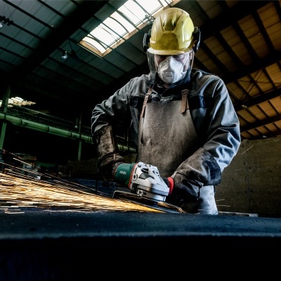 Trabalhador com capacete e máscara a usar esmerilhadora elétrica a produzir faíscas numa oficina