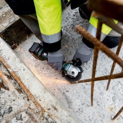 Pessoa a usar esmerilhadora para cortar ferro num canteiro de construção