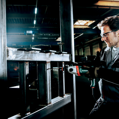 Homem a utilizar furadeira elétrica em estrutura metálica dentro de fábrica