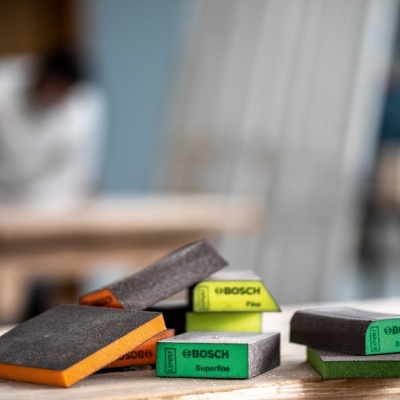 Blocos de lixagem Bosch coloridos sobre uma mesa de madeira, etiquetas com 'Fine' e 'Superfine' visíveis.