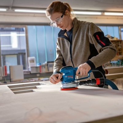 Pessoa a usar lixadora elétrica Bosch azul para lixar madeira clara