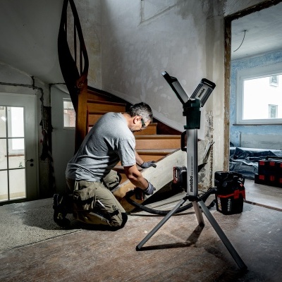 Homem a trabalhar numa escada de madeira em sala em renovação com ferramentas e luz de trabalho