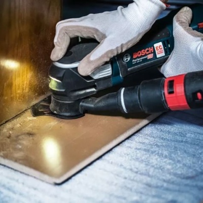 Lixadora elétrica BOSCH a ser usada em superfície de madeira com luvas brancas