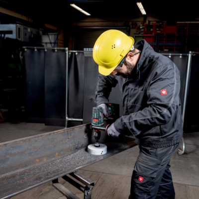 Homem com capacete amarelo lixa peça metálica com esmerilhadora em oficina
