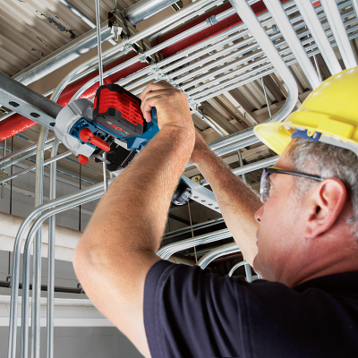 Homem com capacete amarelo usando ferramenta elétrica em estrutura metálica no teto