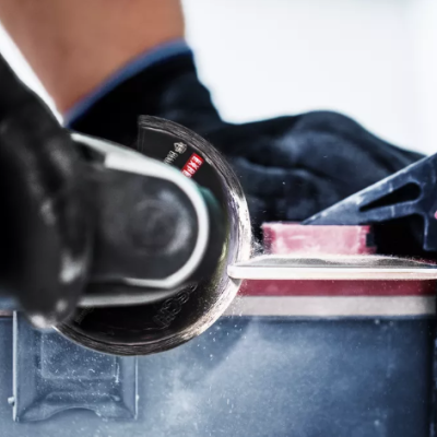 Pessoa usando esmeril para trabalhar numa peça vermelha com luvas pretas.