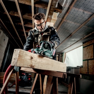Homem a usar lixadora elétrica em tábua de madeira numa oficina