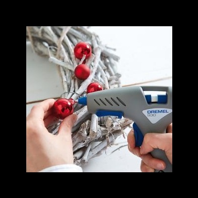 Pistola de cola quente Dremel cinzenta e azul usada para colar bolas vermelhas num suporte de ramos entrelaçados