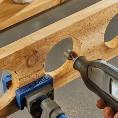 Ferramenta rotativa Dremel a trabalhar em madeira clara com suporte azul e recortes circulares