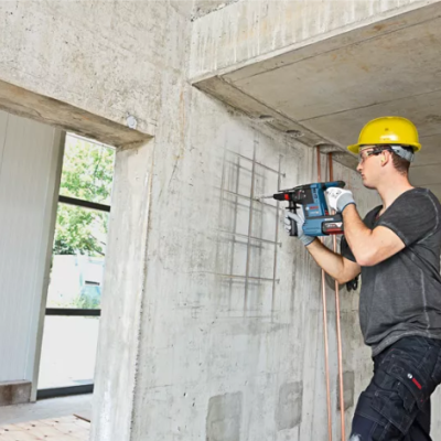 Homem com capacete amarelo utiliza martelete eléctrico para perfurar parede de cimento