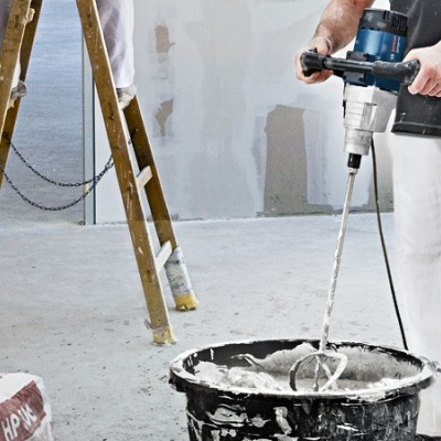 Pessoa a misturar cimento num balde com ferramenta elétrica junto a uma escada de madeira