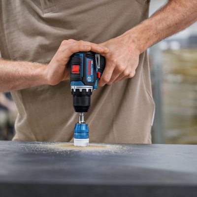 Furadeira/parafusadora a bateria Bosch preta e azul a perfurar superfície cinza