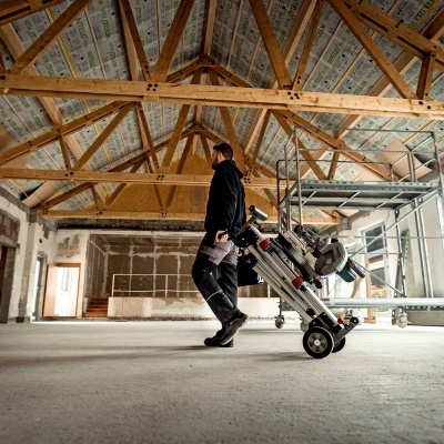 Homem a transportar ferramenta elétrica sobre rodas em espaço interior em construção