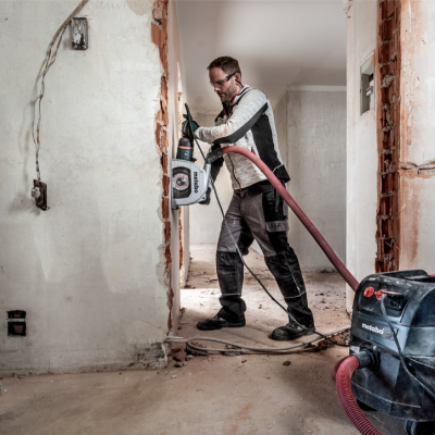 Homem a usar ferramenta elétrica ligada a aspirador Metabo em obra de construção