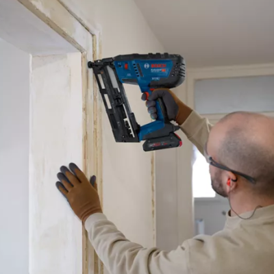 Homem a usar ferramenta elétrica para pregos numa moldura de porta em ambiente interior