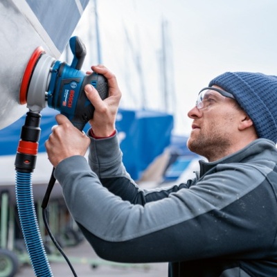 Homem a usar polidora eléctrica numa embarcação branca num estaleiro náutico