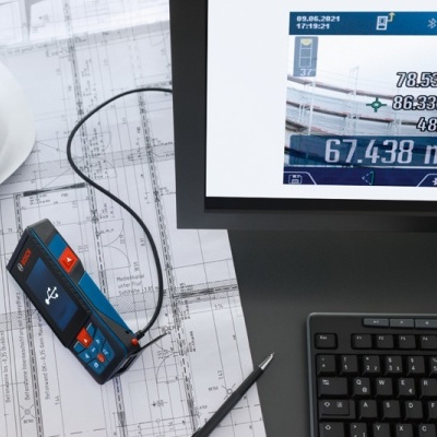 Dispositivo medidor a laser sobre plantas arquitetónicas ao lado de capacete branco e computador com teclado