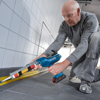 Homem a usar ferramenta para aplicar silicone amarelo entre chão e parede azulejada