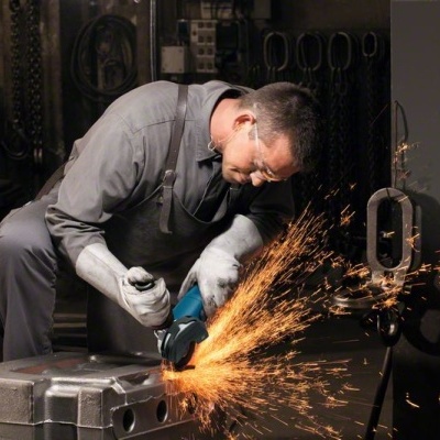 Pessoa a usar esmerilhadora elétrica para cortar peça metálica com fagulhas em oficina