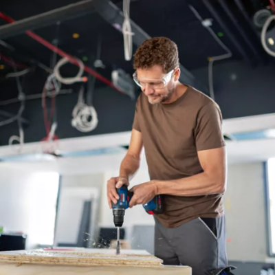 Homem a usar furadeira numa superfície de madeira em ambiente interior