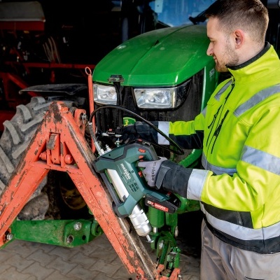 Homem usando pistola de pregos verde perante trator em oficina