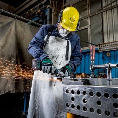Trabalhador com capacete amarelo opera ferramenta elétrica numa oficina