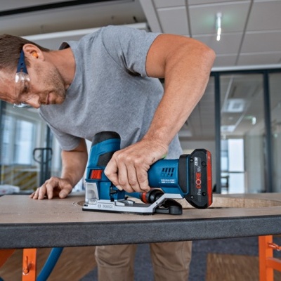 Homem a cortar madeira com serra elétrica azul e preta numa oficina