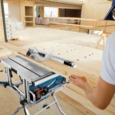 Máquina de serra circular portátil com base metálica e pessoa a segurar tábua de madeira em construção interior