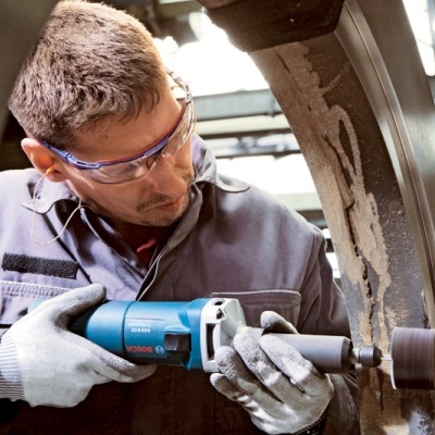 Homem a usar ferramenta elétrica azul para trabalho em metal numa oficina industrial.