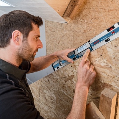 Homem usando nível digital para verificar alinhamento em madeira numa obra interior