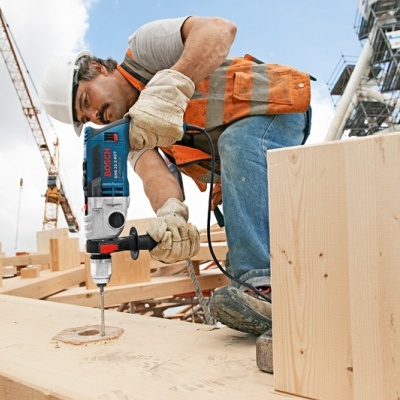Homem a usar broca elétrica Bosch em tábua de madeira numa obra