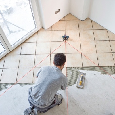 Pessoa a instalar azulejos de cerâmica bege no chão de uma divisão interior