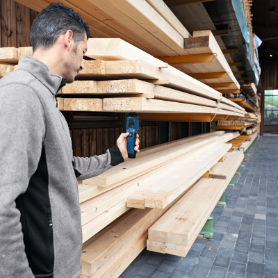Homem mede humidade de tábuas de madeira em prateleiras numa estrutura de armazenamento
