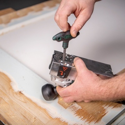 Pessoa a ajustar ferramenta elétrica numa superfície branca com moldura de madeira