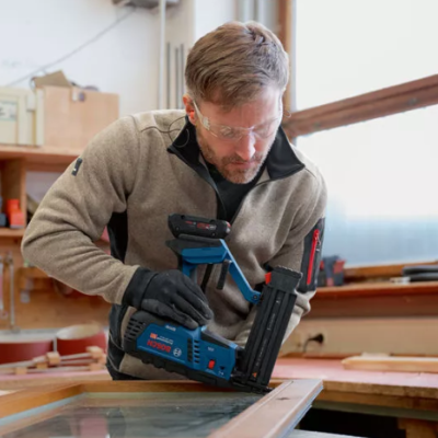 Homem a usar pistola aplicadora de pregos numa janela de madeira numa oficina