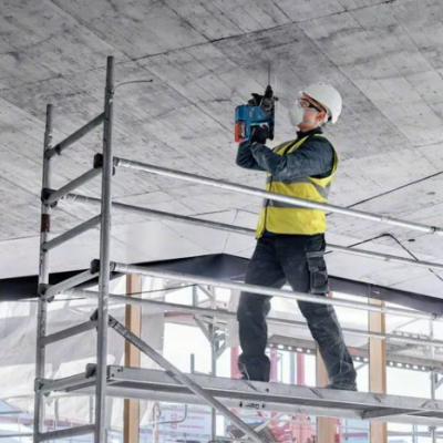 Trabalhador de construção em andaime a perfurar teto de betão