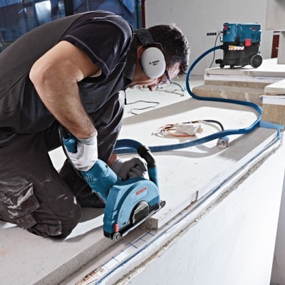 Pessoa a usar máquina de corte elétrica azul com proteção auditiva num ambiente de construção