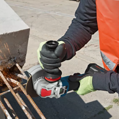 Pessoa com colete laranja usando esmerilhadora para cortar ferro armado em betão