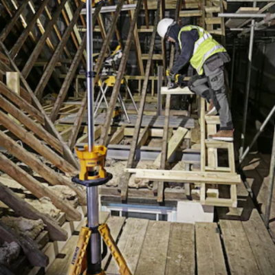 Tripé amarelo de medição em obra com trabalhador em escada próxima