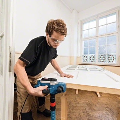 Homem a usar ferramenta elétrica para trabalhar em madeira branca numa bancada interior