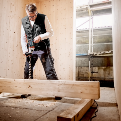 Homem a furar um tronco de madeira numa oficina com paredes de madeira clara