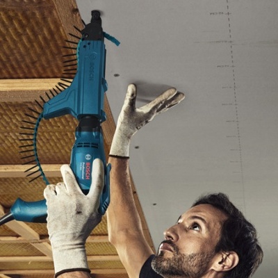 Homem com luvas segurando furadeira azul para instalação de teto de madeira