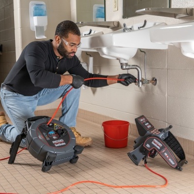 Homem a desentupir canalização com equipamento Outil Detecta junto a lavatório branco
