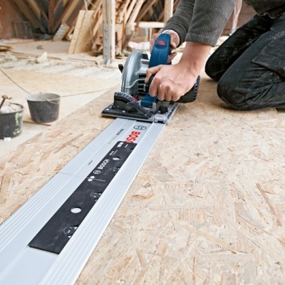 Máquina de corte circular BOSCH azul e preta com guia metálica sobre madeira OSB