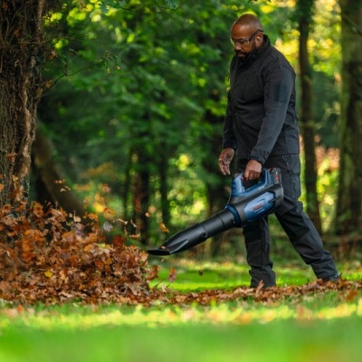 Homem com fato preto usando soprador de folhas azul e preto numa área exterior verde