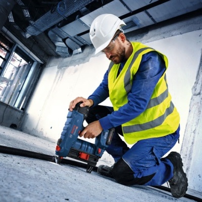 Trabalhador com capacete branco usando furadeira azul dentro de sala em construção