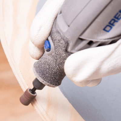 Ferramenta elétrica Dremel cinzenta com ponta abrasiva a trabalhar madeira clara