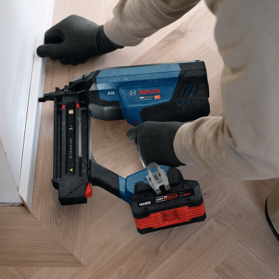 Aparelho pneumático de pregos Bosch Pro azul e preto em piso de madeira claro próximo de uma parede branca