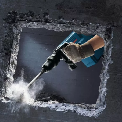 Martelo perfurador elétrico a perfurar parede de cimento com mão enluvada.